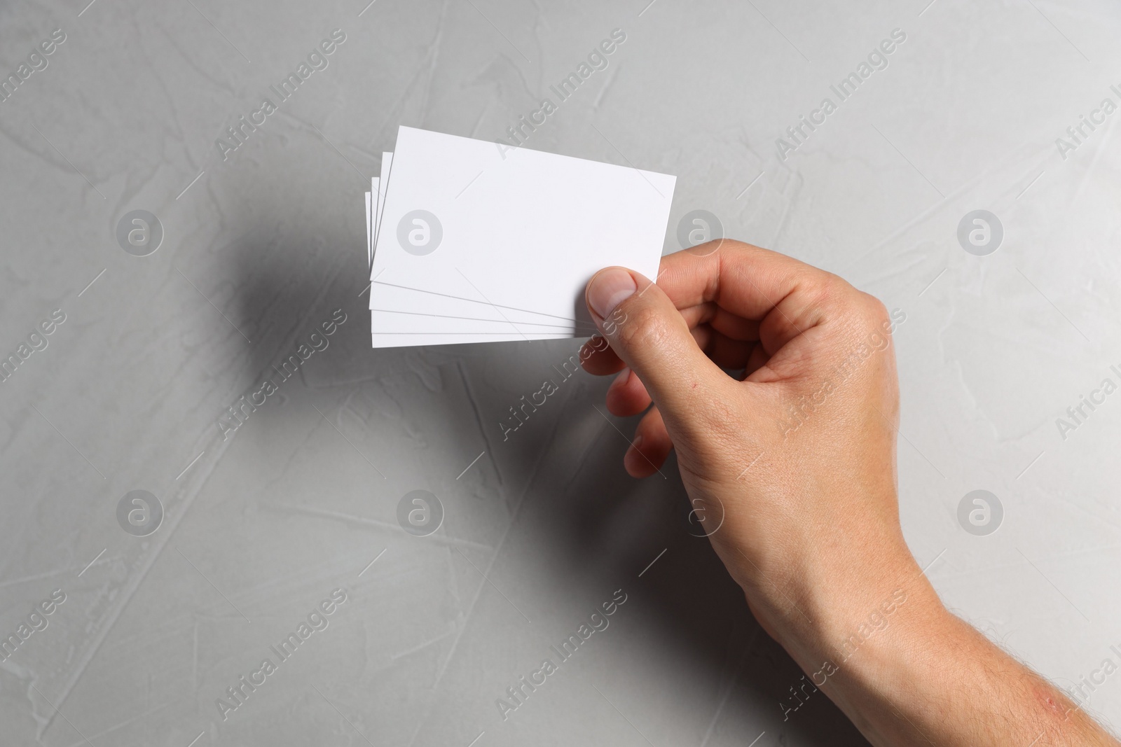 Photo of Man holding white blank cards at light grey table, top view. Mockup for design