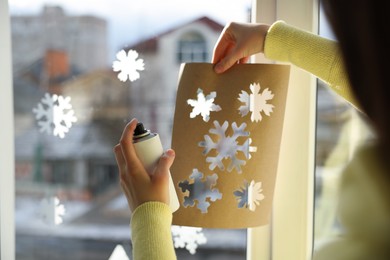 Photo of Woman using snow spray for decorating window with snowflakes at home, closeup