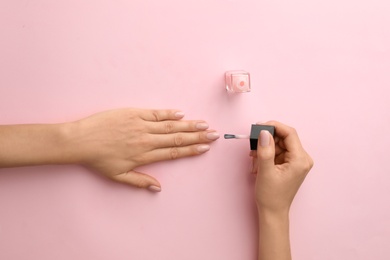 Woman applying nail polish on color background, top view