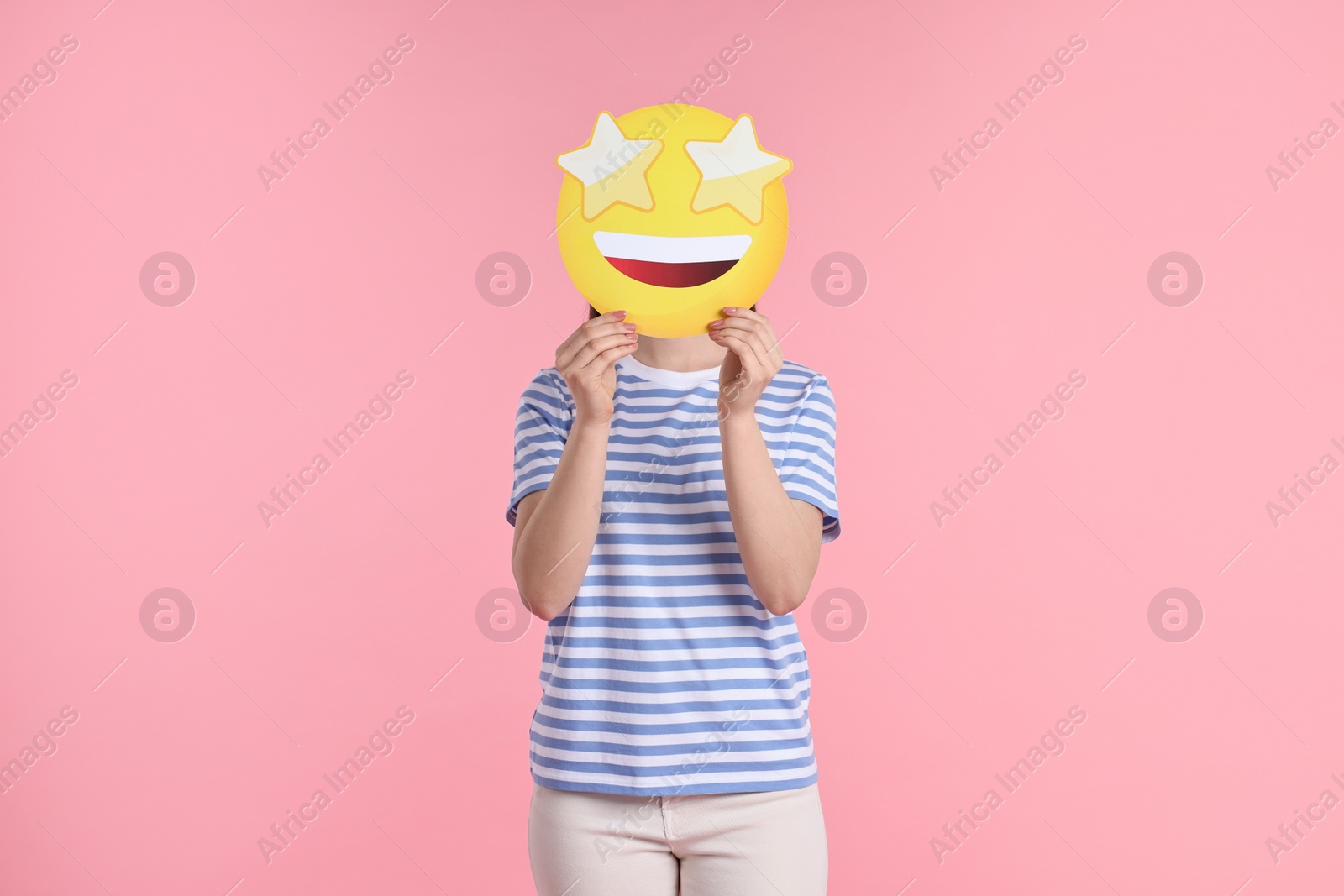 Photo of Woman holding emoticon with stars instead of eyes on pink background