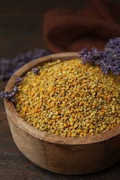 Photo of Fresh bee pollen granules in bowl and lavender on wooden table, closeup