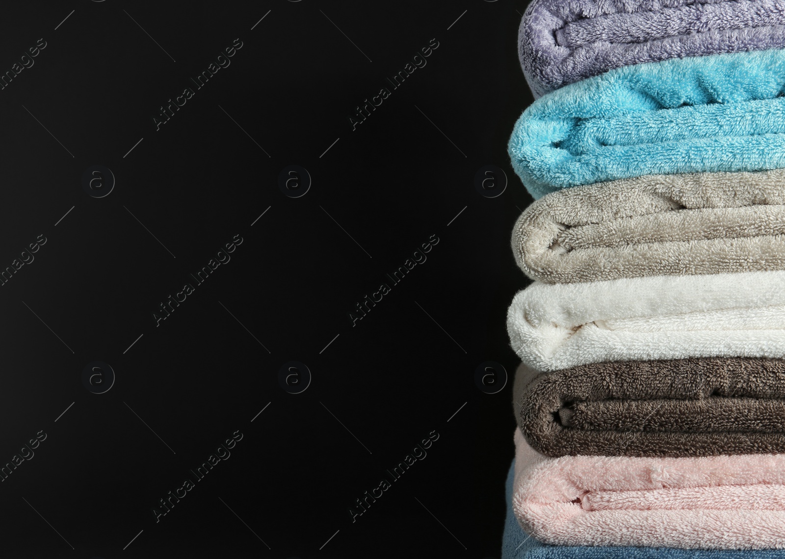 Photo of Different fresh soft terry towels on dark background. Space for text