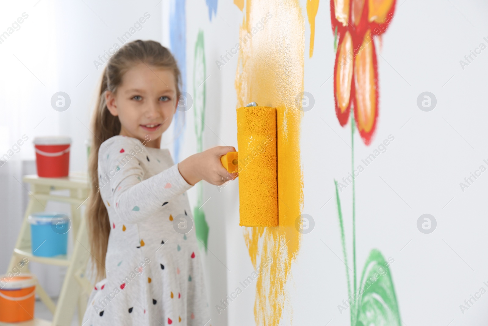 Photo of Little child painting wall with roller brush indoors