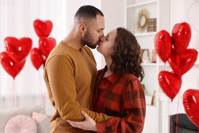 Lovely couple kissing in room decorated with heart shaped air balloons. Valentine's day celebration