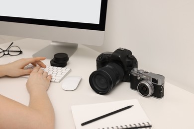 Photographer working on computer at white table with cameras indoors, closeup