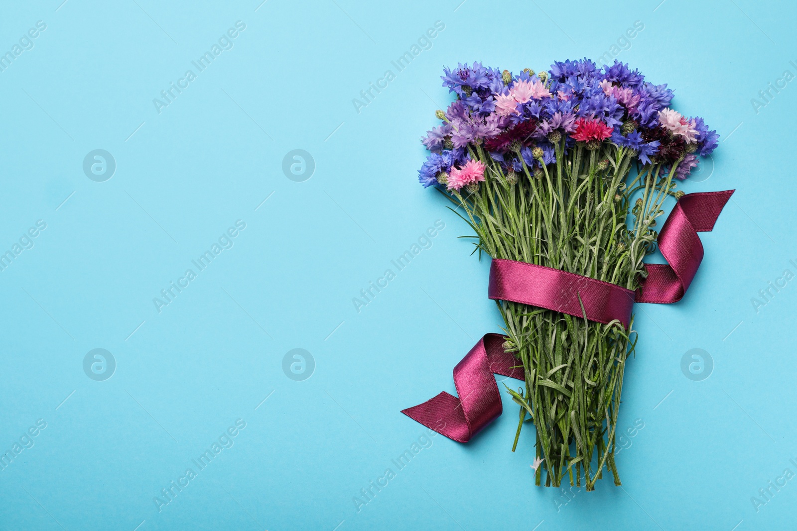 Photo of Bouquet of beautiful cornflowers on light blue background, top view. Space for text