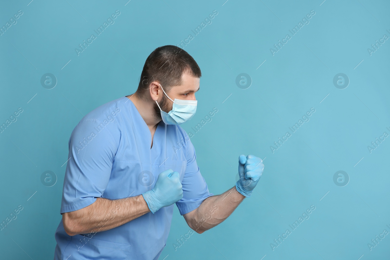 Photo of Doctor with protective mask in fighting pose on light blue background, space for text. Strong immunity concept