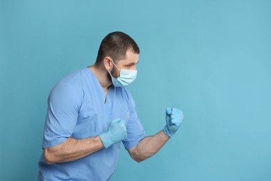 Doctor with protective mask in fighting pose on light blue background, space for text. Strong immunity concept