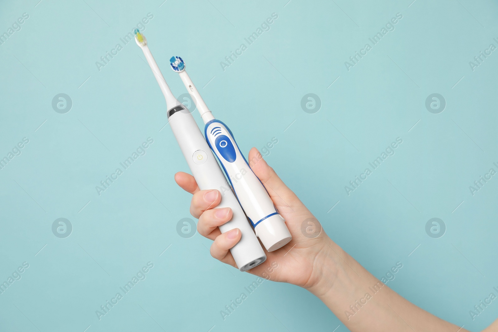 Photo of Woman holding electric toothbrushes on light blue background, closeup