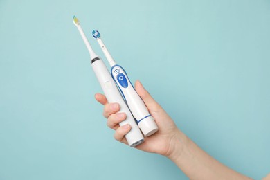 Photo of Woman holding electric toothbrushes on light blue background, closeup