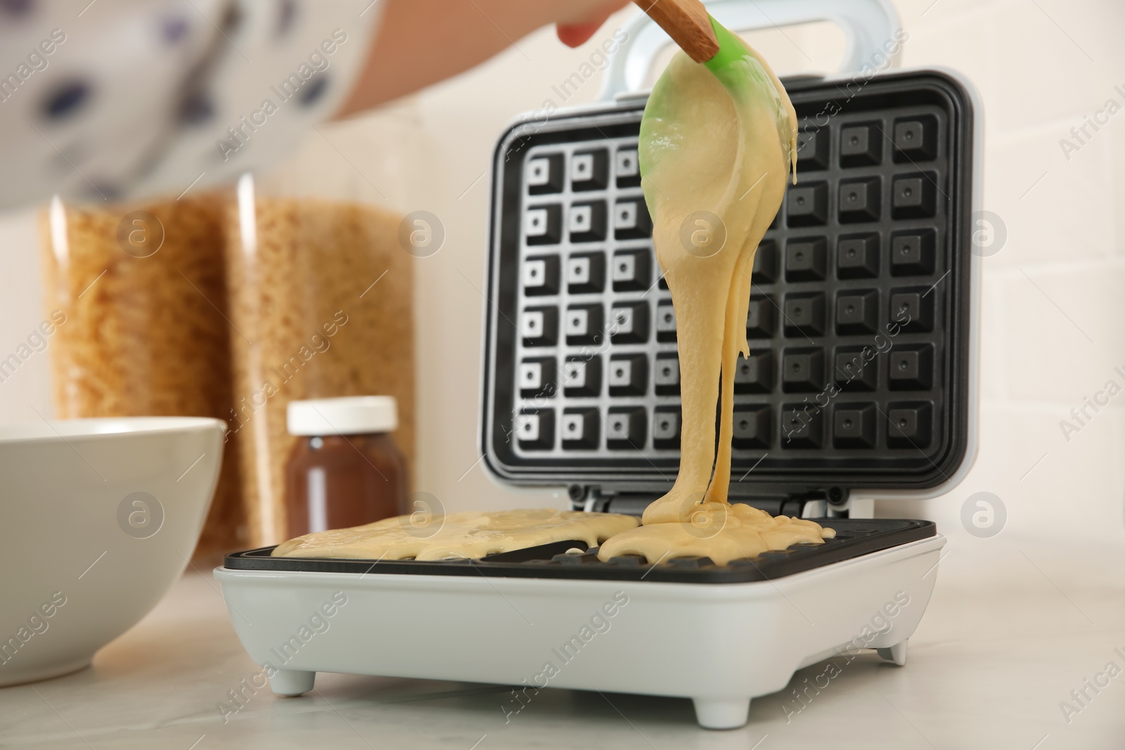 Photo of Woman pouring dough onto Belgian waffle maker in kitchen, closeup