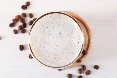 Refreshing iced coffee with milk in glass and beans on white table, top view