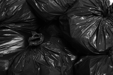 Photo of Black trash bags full of garbage as background, top view