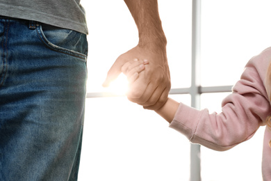 Father holding hands with his child indoors, closeup. Happy family