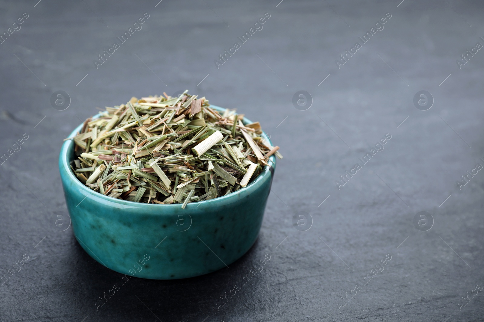 Photo of Bowl with aromatic dried lemongrass on black table. Space for text