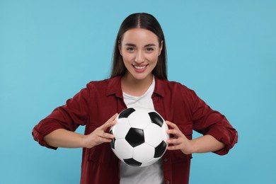 Happy fan holding soccer ball on light blue background