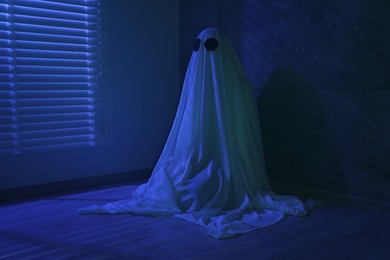 Photo of Creepy ghost. Woman covered with sheet near window in blue light