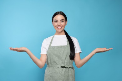 Photo of Young woman in grey apron on light blue background,