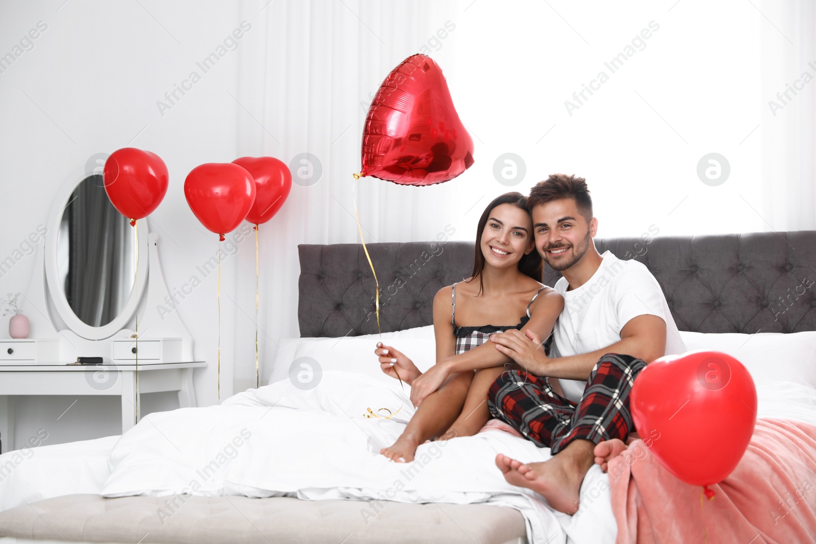 Photo of Young couple in bedroom decorated with air balloons. Celebration of Saint Valentine's Day