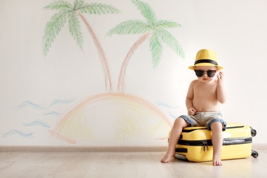 Photo of Adorable little child playing traveler with suitcase indoors