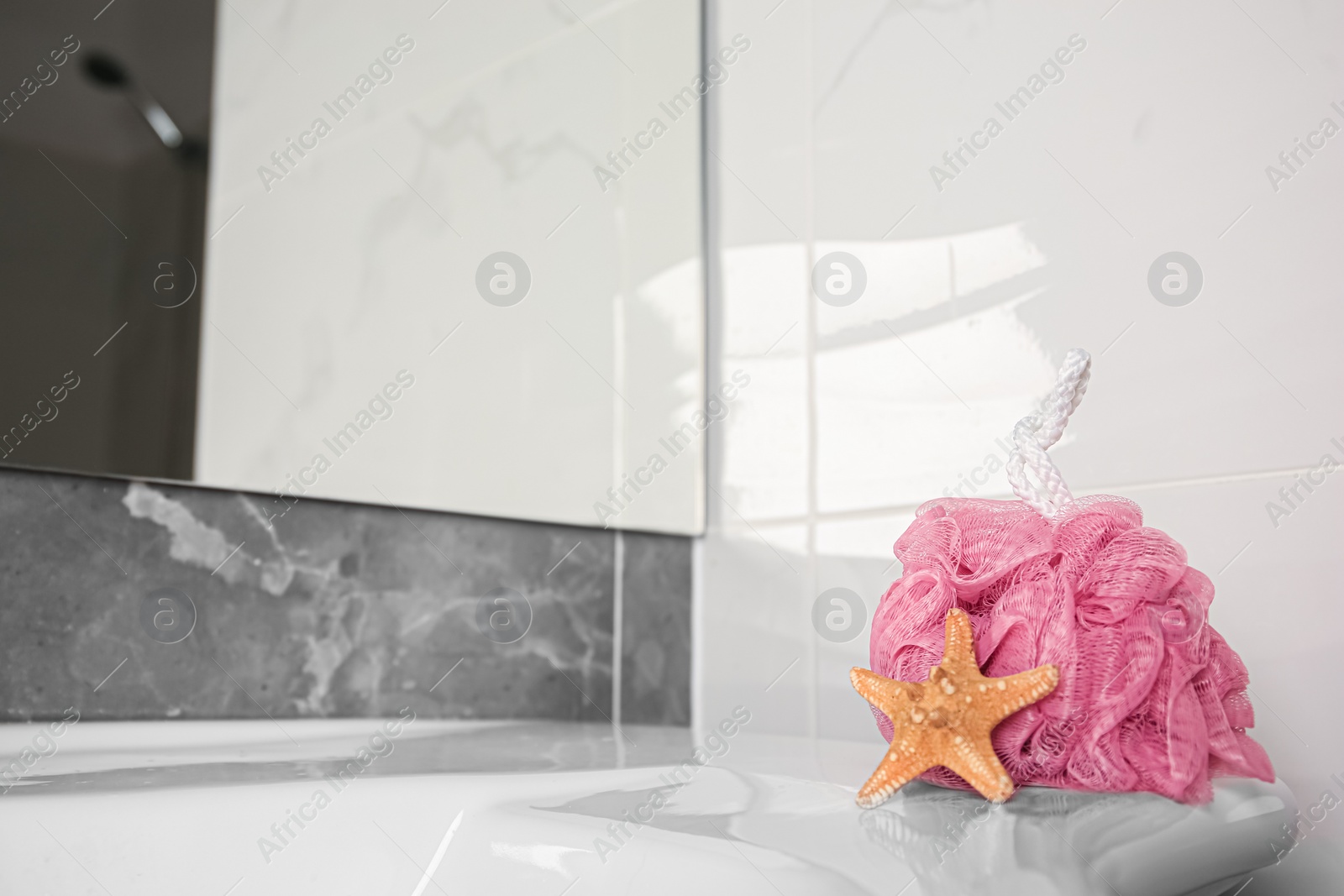 Photo of Pink shower puff and starfish on washbasin in bathroom, space for text