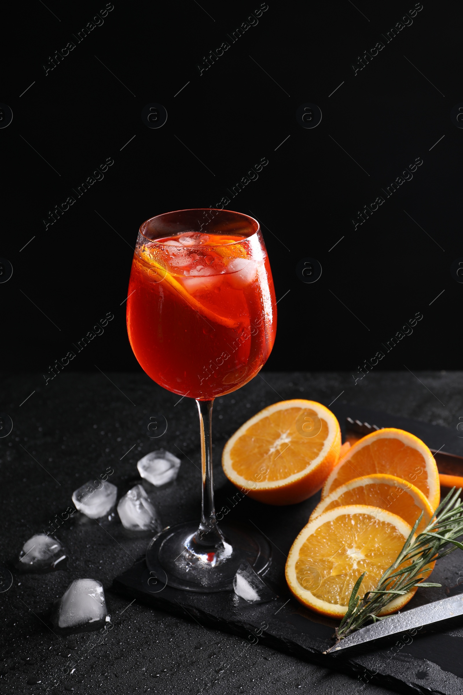 Photo of Glass of tasty Aperol spritz cocktail with orange slices, ice cubes and rosemary on table against black background