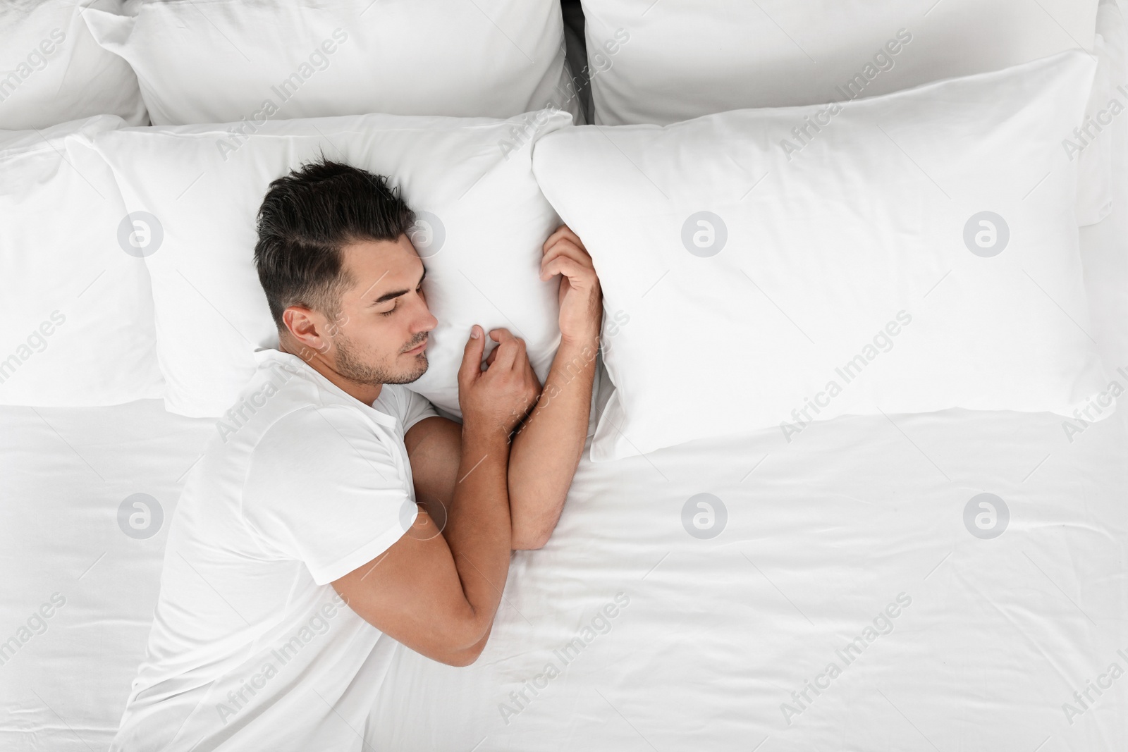 Photo of Young man sleeping on bed with soft pillows at home, top view