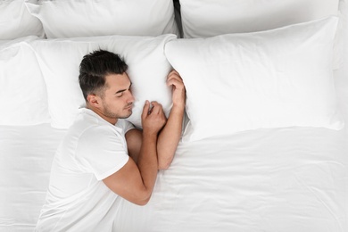 Young man sleeping on bed with soft pillows at home, top view