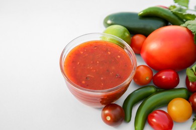 Photo of Bowl with delicious salsa sauce and ingredients on white background, closeup. Space for text