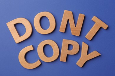 Photo of Plagiarism concept. Phrase Don't Copy made of wooden letters on blue background, top view
