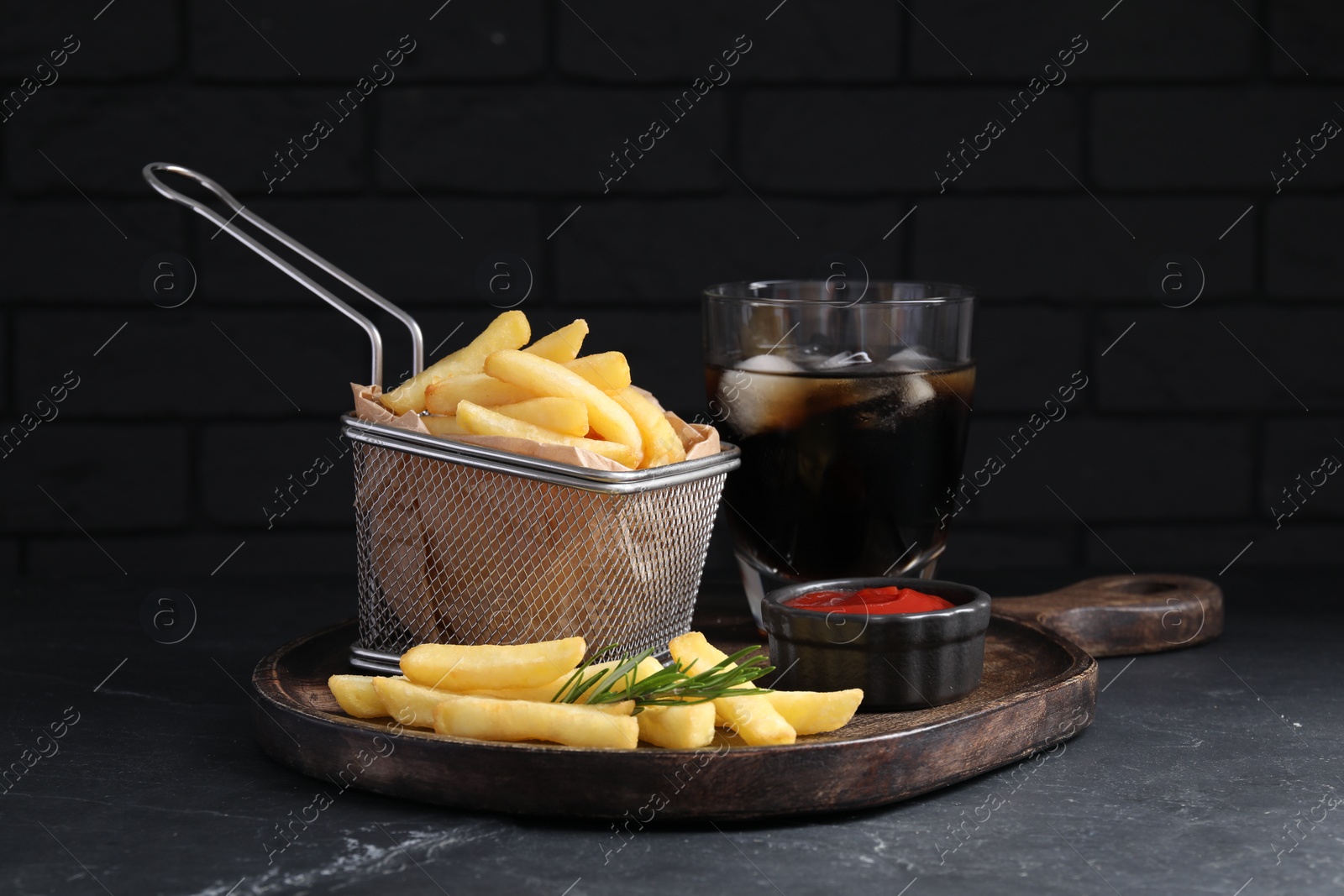 Photo of Tasty french fries, ketchup and soda drink on black table against brick wall