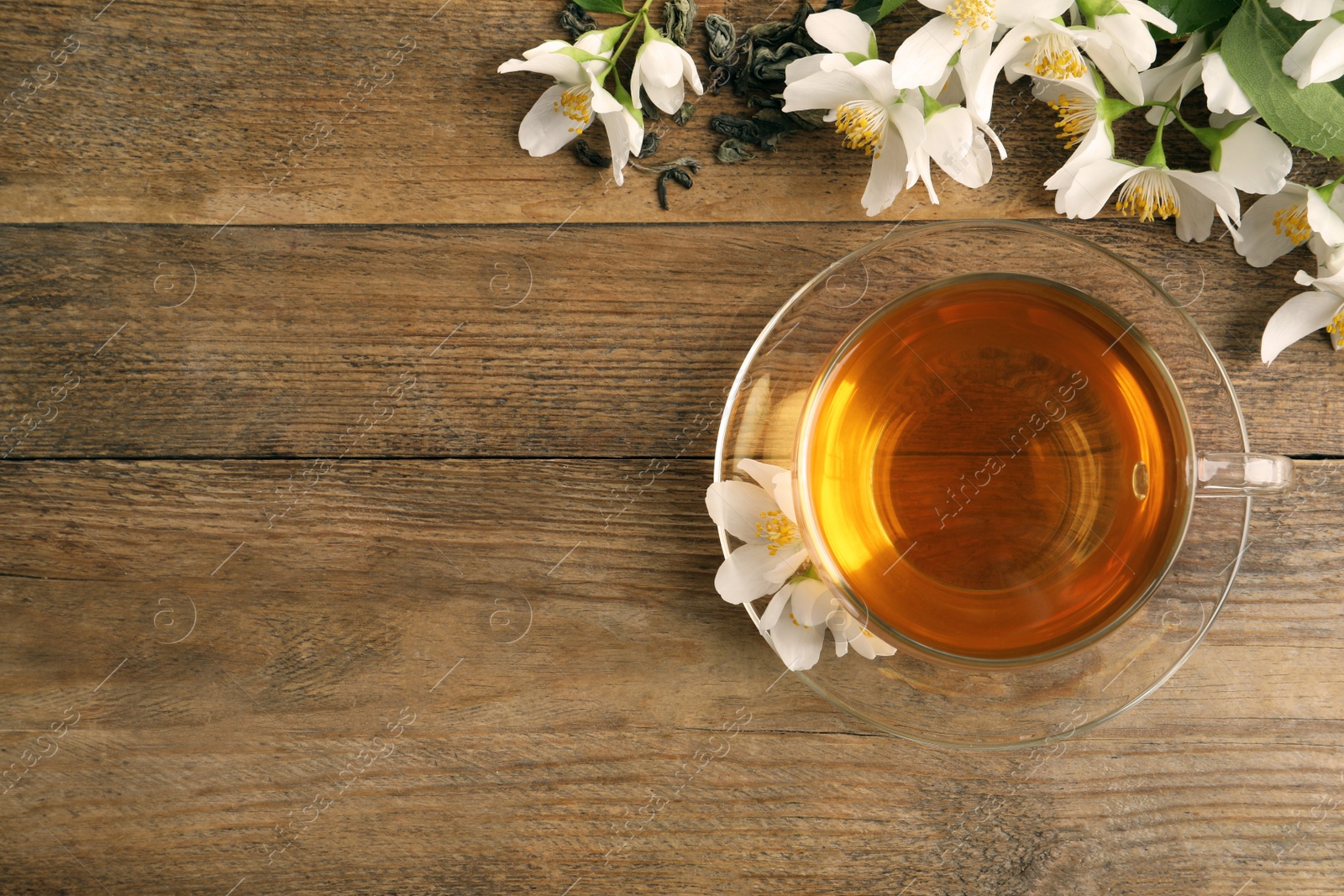 Photo of Glass cup of aromatic jasmine tea and fresh flowers on wooden table, flat lay. Space for text