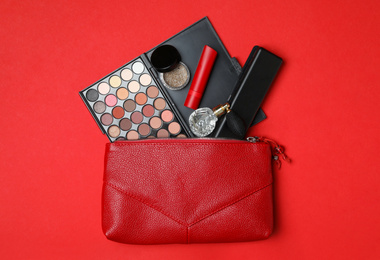 Photo of Cosmetic bag with makeup products and perfume on red background, flat lay