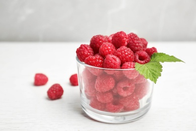 Photo of Glass with ripe aromatic raspberries on table