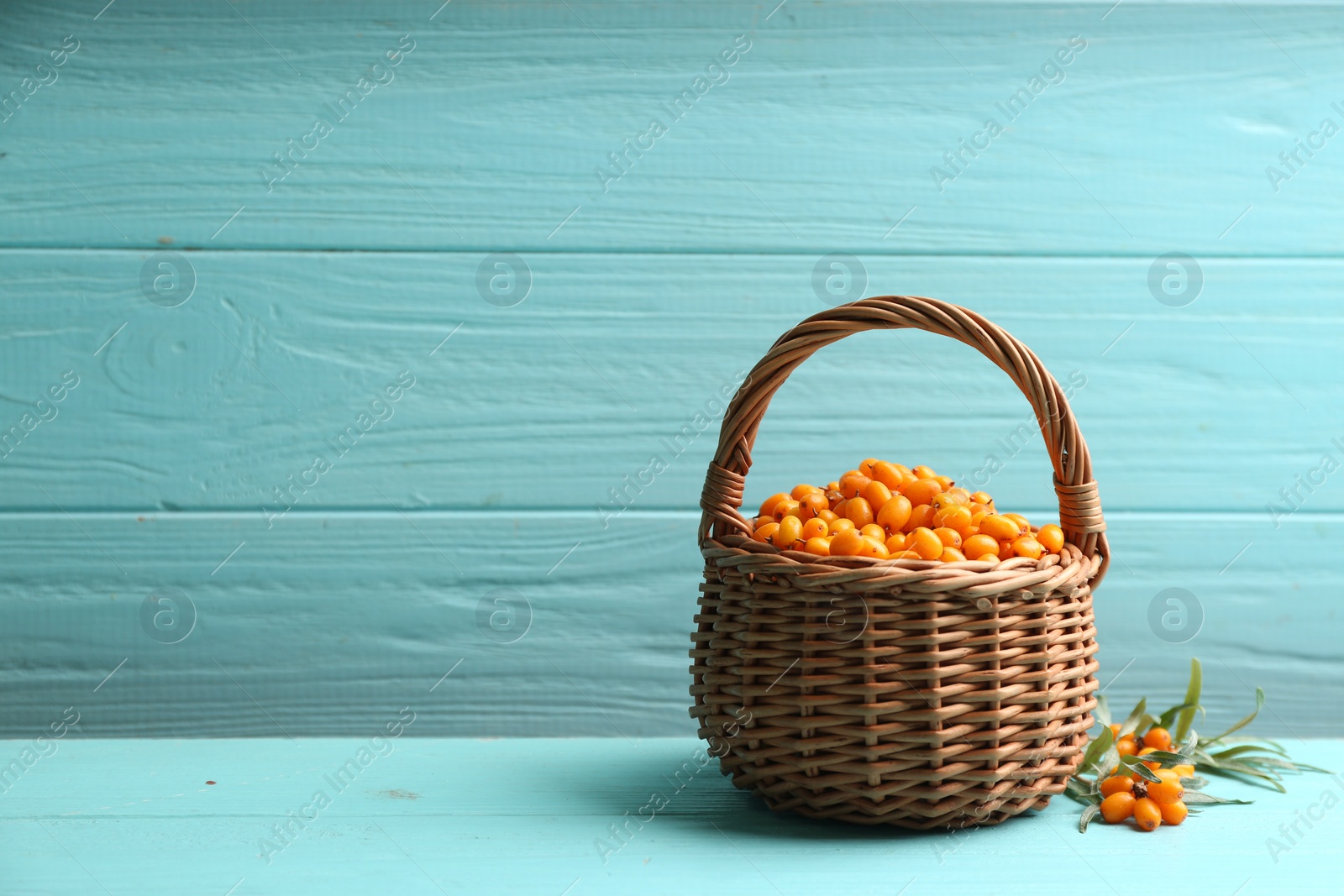 Photo of Fresh ripe sea buckthorn in wicker basket on light blue wooden table. Space for text