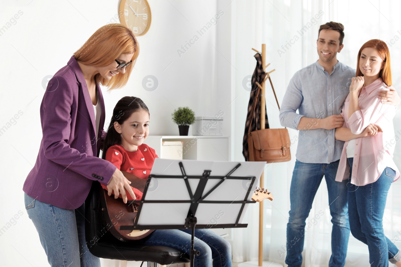 Photo of Little girl with her teacher and parents at music lesson. Learning notes