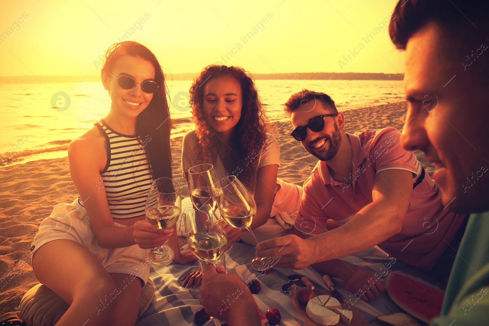 Image of Group of friends having picnic near river at sunset