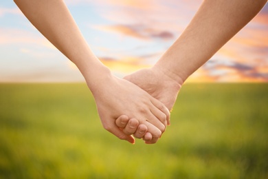 Young lovely couple holding hands in green field, closeup