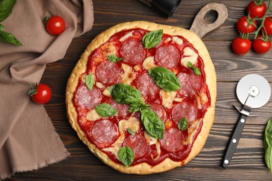 Photo of Pita pizza with pepperoni, cheese, basil and tomatoes on wooden table, flat lay