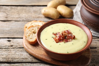 Photo of Tasty potato soup with bacon in bowl and cut bread on wooden table