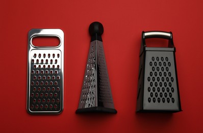 Different modern graters on red background, flat lay
