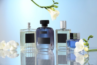 Photo of Luxury perfumes and freesia flowers on mirror surface against light blue background. Floral fragrance