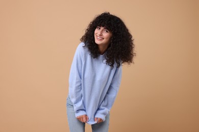 Happy young woman in stylish light blue sweater on beige background