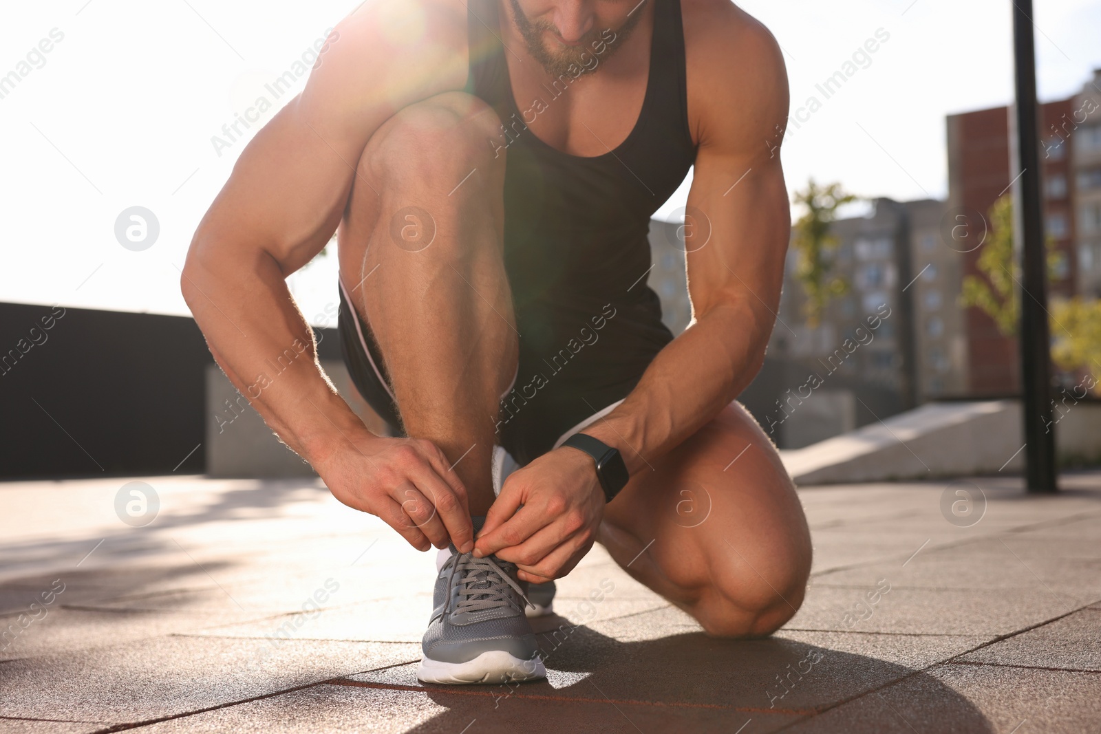 Photo of Man tying shoelaces before running outdoors on sunny day, closeup