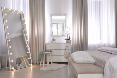Large mirror with light bulbs and chest of drawers in bedroom. Interior design