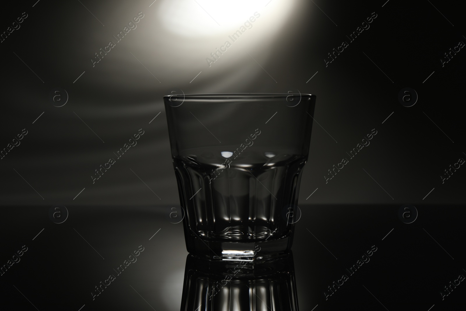 Photo of One empty glass on mirror surface against dark background