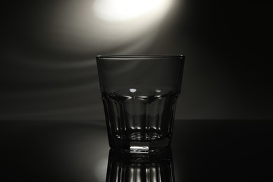 Photo of One empty glass on mirror surface against dark background