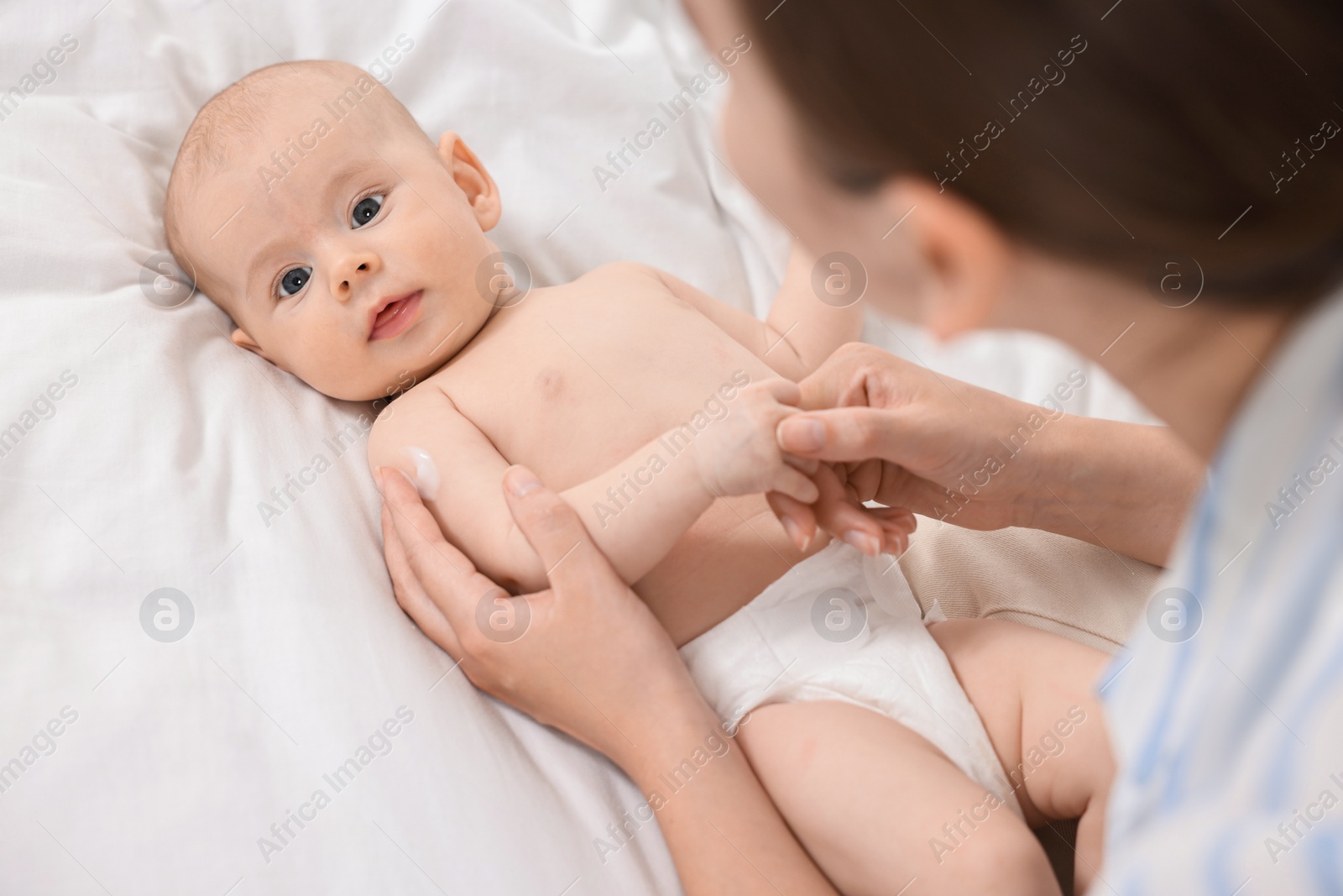 Photo of Woman applying body cream onto baby`s skin on bed, above view