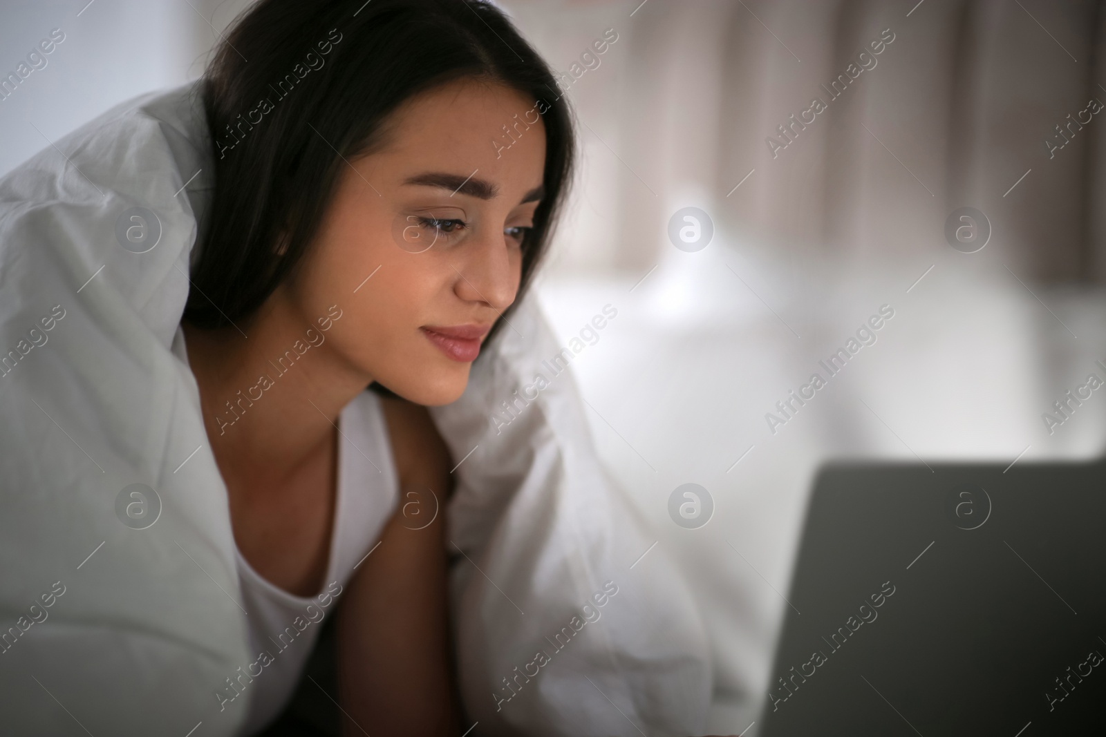 Photo of Young woman with nomophobia using laptop in bed at night. Insomnia concept