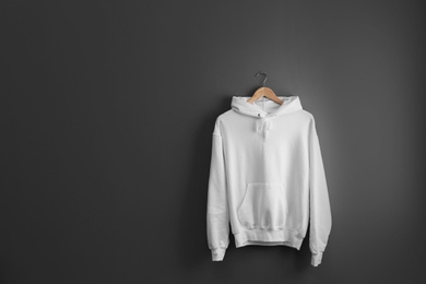 Photo of New hoodie sweater with hanger on grey wall. Mockup for design